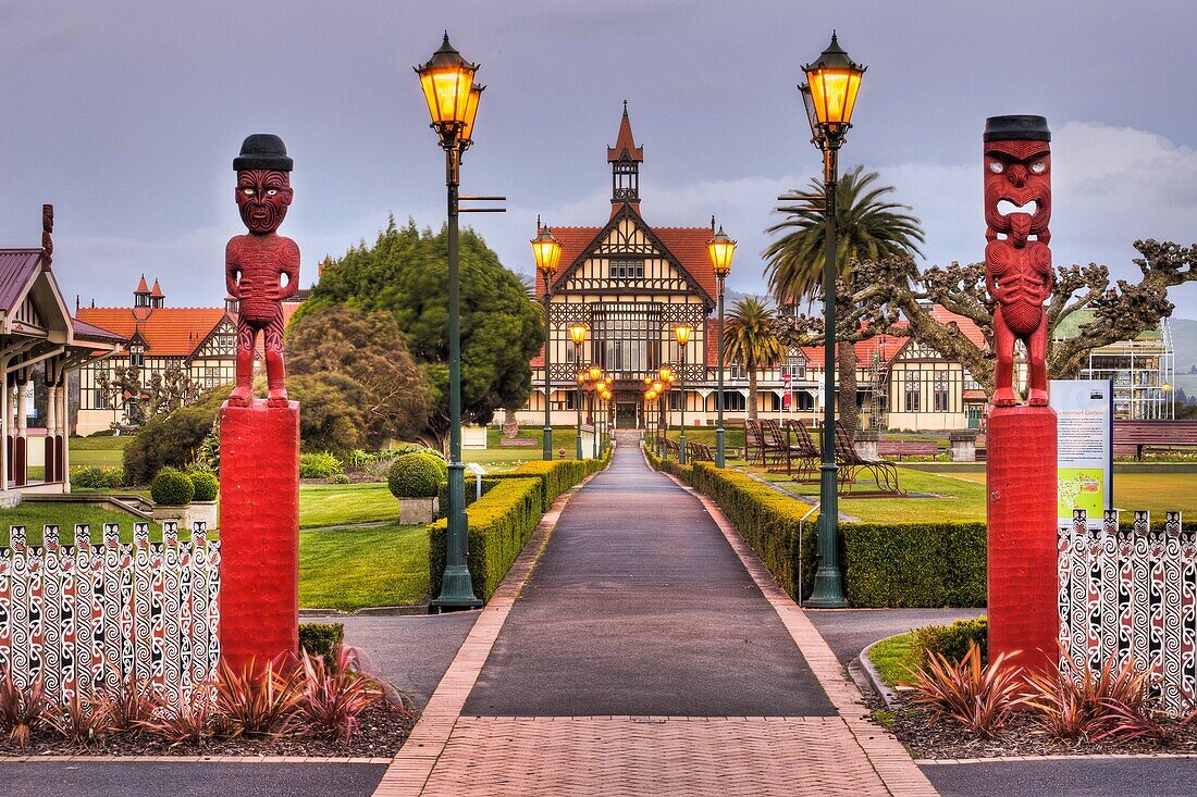 Rotorua Museum entrance pathway lined by lamps and Maori wooden carved figures, dusk, Government gardens, Rotorua