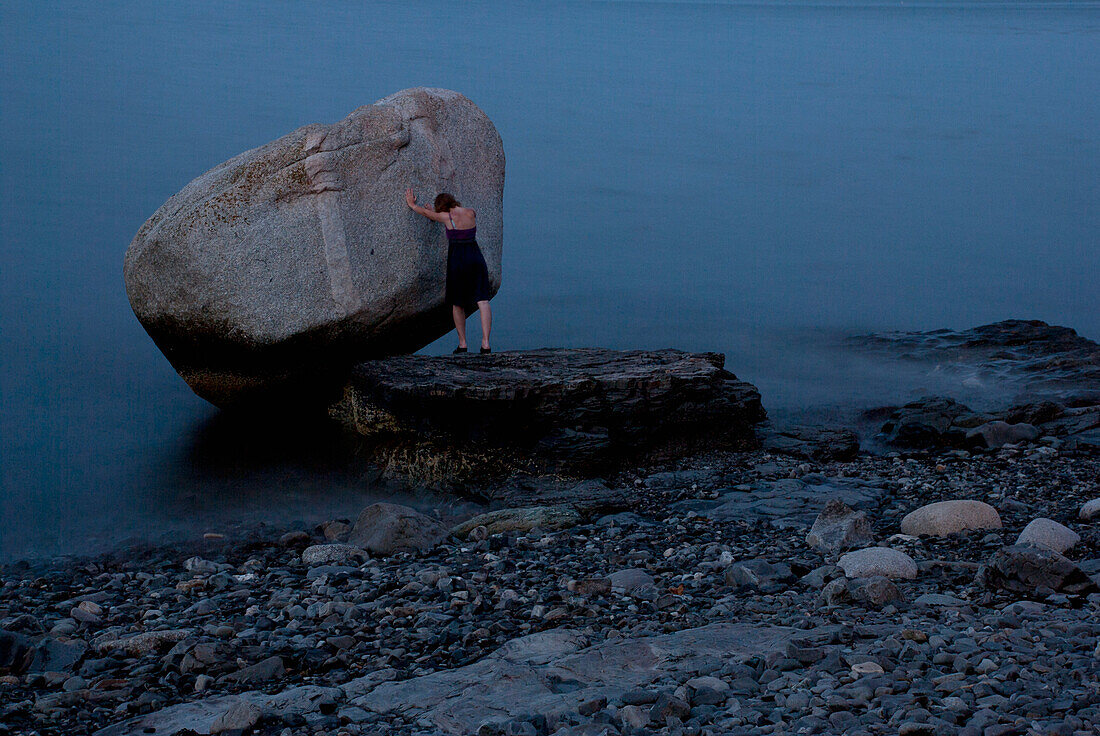 Young Woman Pushing Against Large Rock in Water, Bar Harbor, Maine, USA
