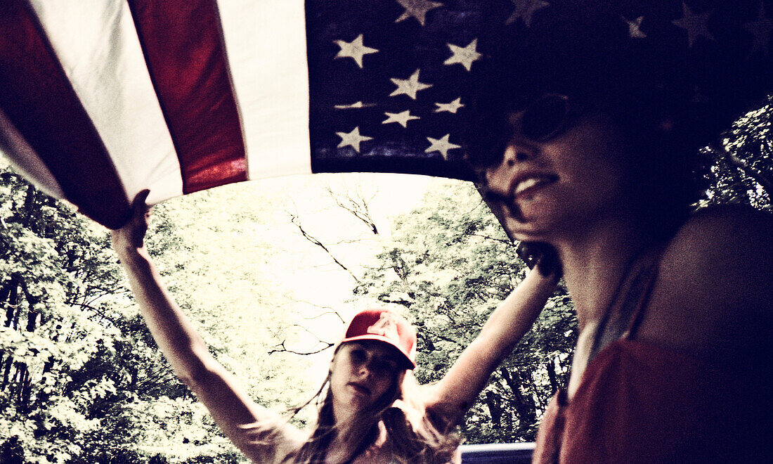 Two Young Women Underneath American Flag in Back of Pickup Truck