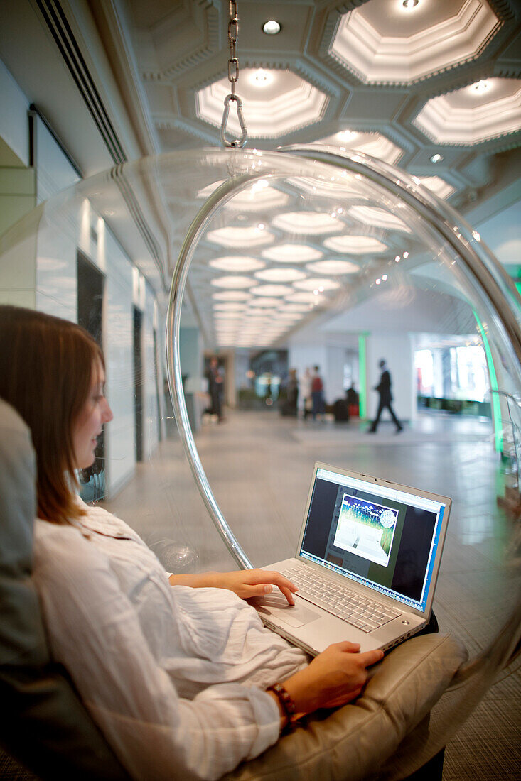 Woman sitting in a hanging ball chair while using a laptop, hotel lobby, Brussels, Belgium