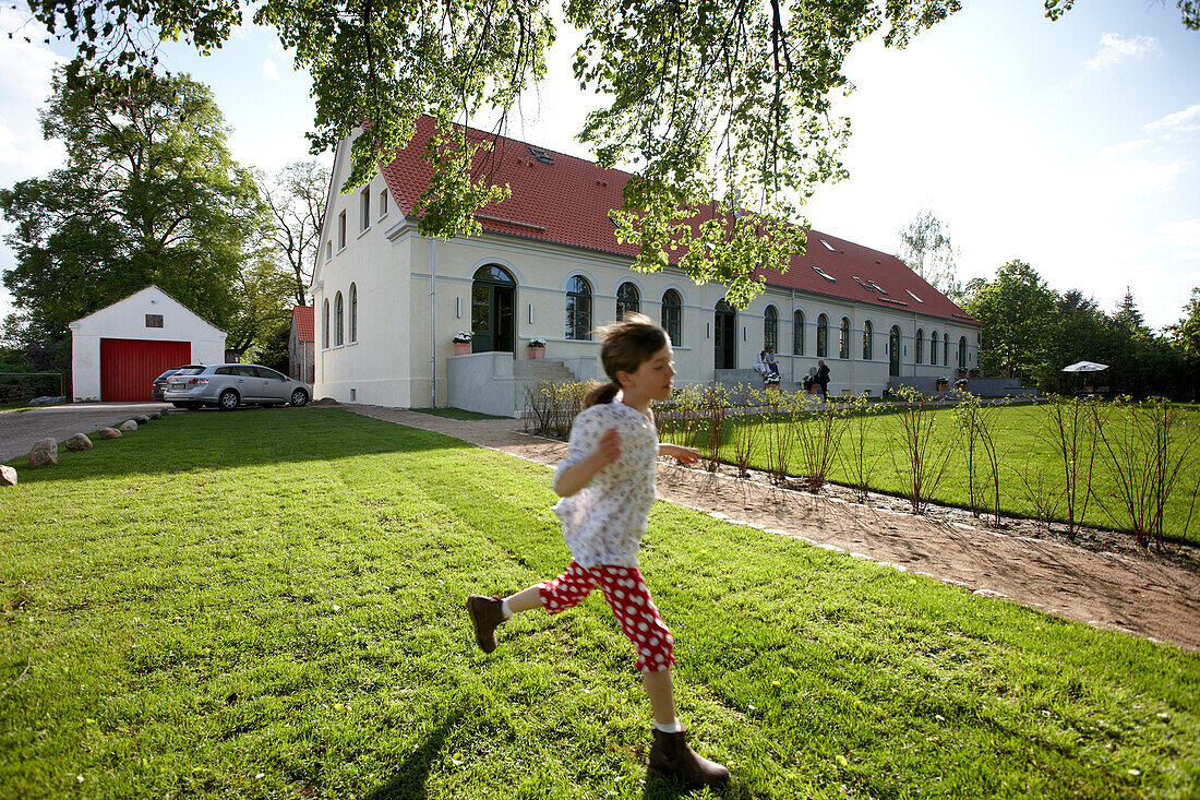 Girl running over a meadow near an hotel, Fincken, Mecklenburg-Western Pomerania, Germany