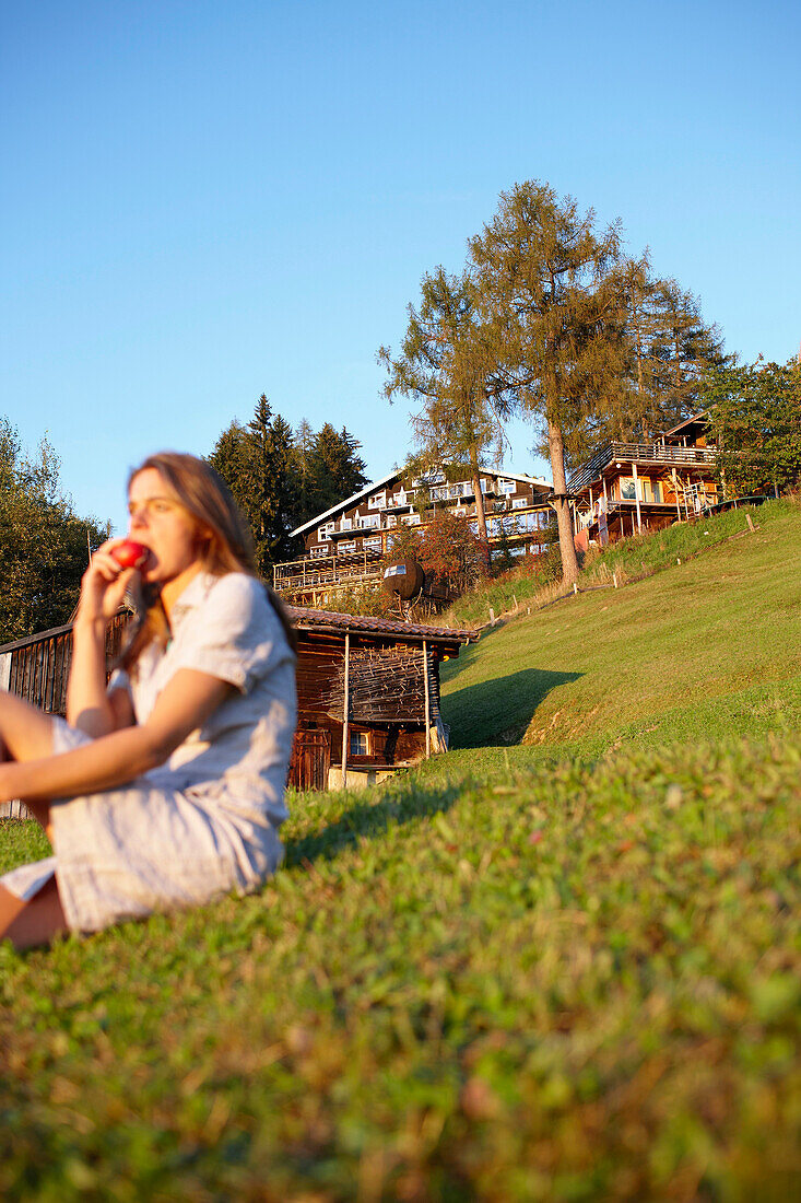 Woman sitting on grass while eating an apple, Am Hochpillberg, Schwaz, Tyrol, Austria