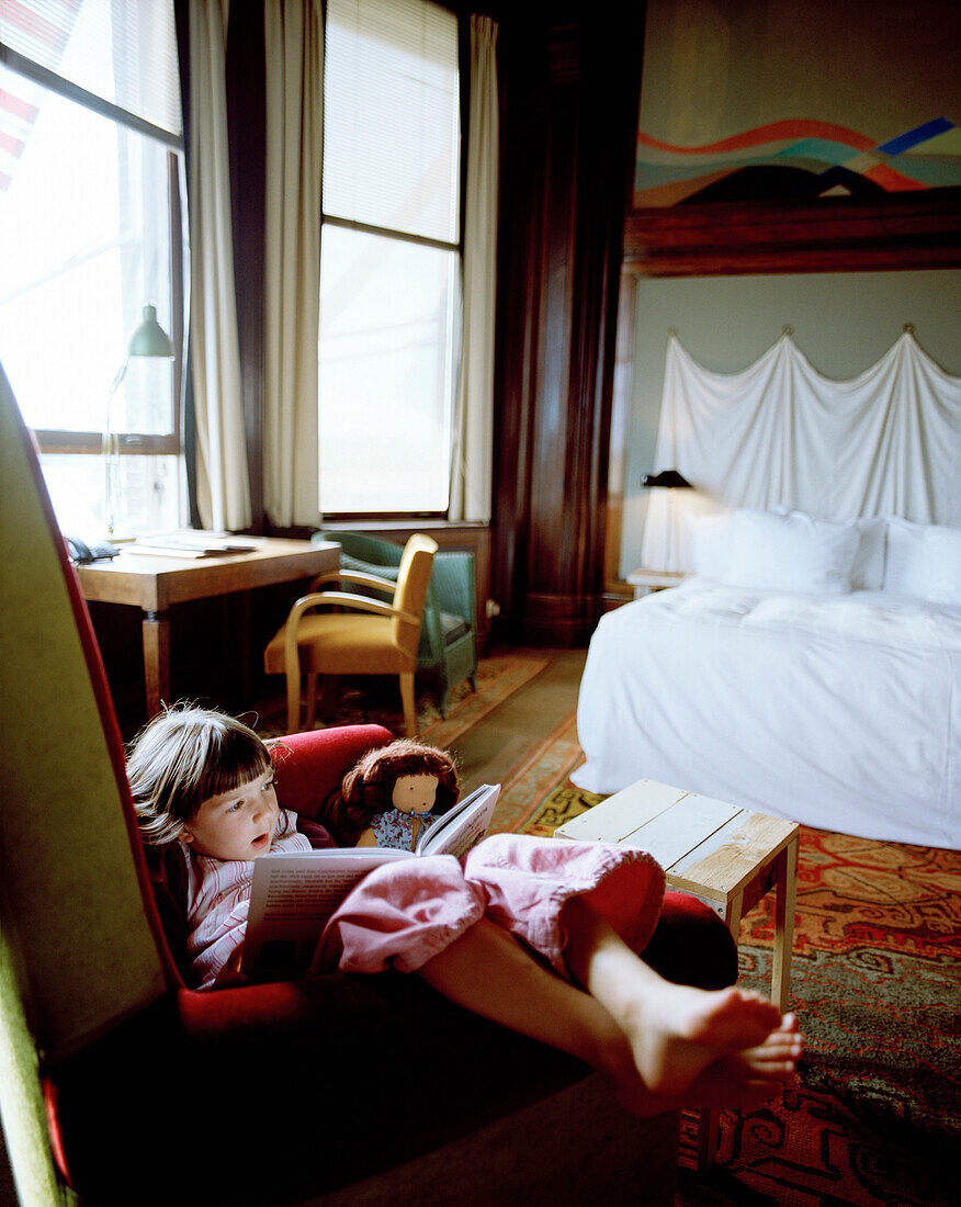 Girl sitting in an armchair while reading a book in a hotel room, Rotterdam, Netherlands