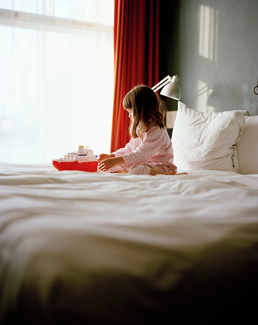 Mädchen spielt mit einem Schiff auf einem Hotelbett, Hotel New York, Kop van Zuid, Rotterdam, Niederlande