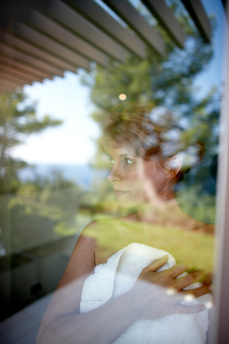 Woman wrapped in a towel looking out of a hotel window, Ramatuelle, Provence-Alpes-Cote d'Azur, France