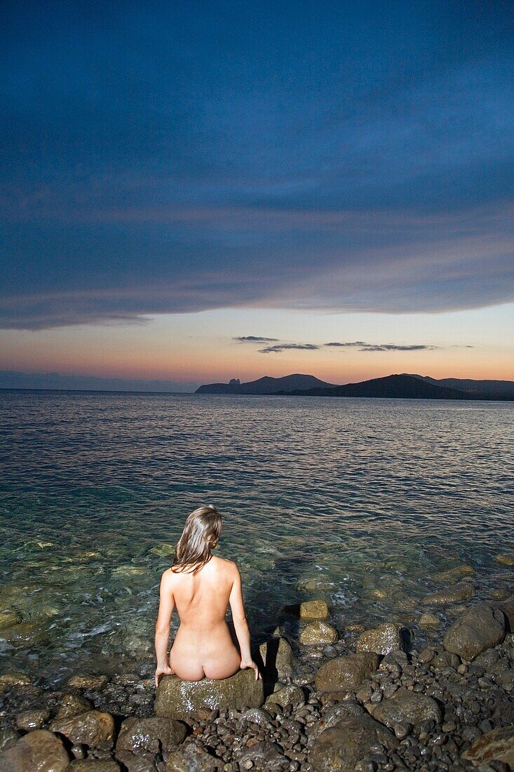 Back view of a naked woman sitting und looking at the sunset