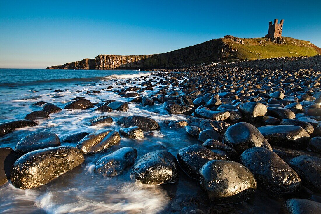 Dunstanburgh Castle, with basalt boulders on beach, autumn, Northumberland, England