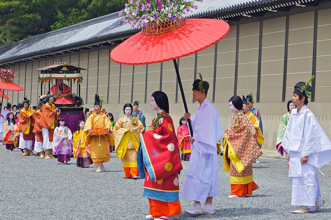 Costumed participants in the parade, some carrying red parasols for ladies walking beside them with the Imperial Palace in the background