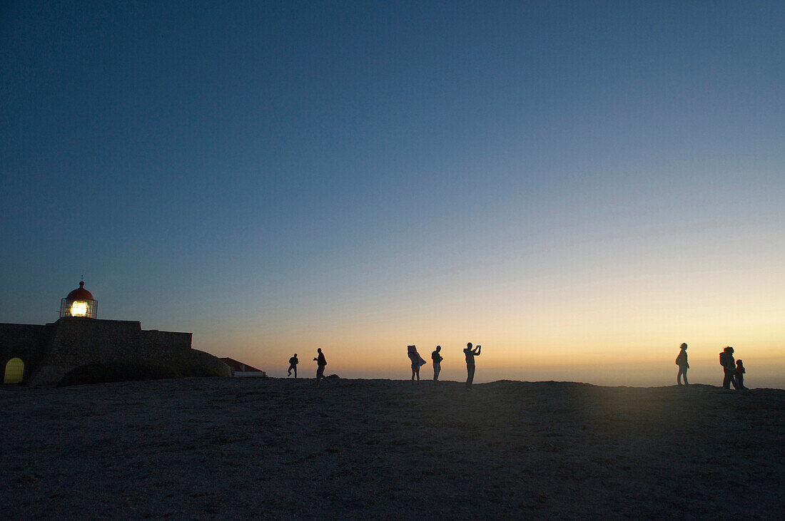Leuchtturm und Menschen als Silhouetten auf hohen Klippen, Cabo de Sao Vicente, nach Sonnenuntergang, Algarve, Portugal, Europa