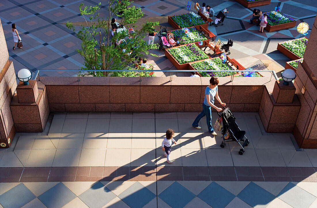A young Japanese mother and her toddler stroll through the sunny multi-level plaza at Yebisu Garden Place in the Ebisu district of Tokyo, Japan.