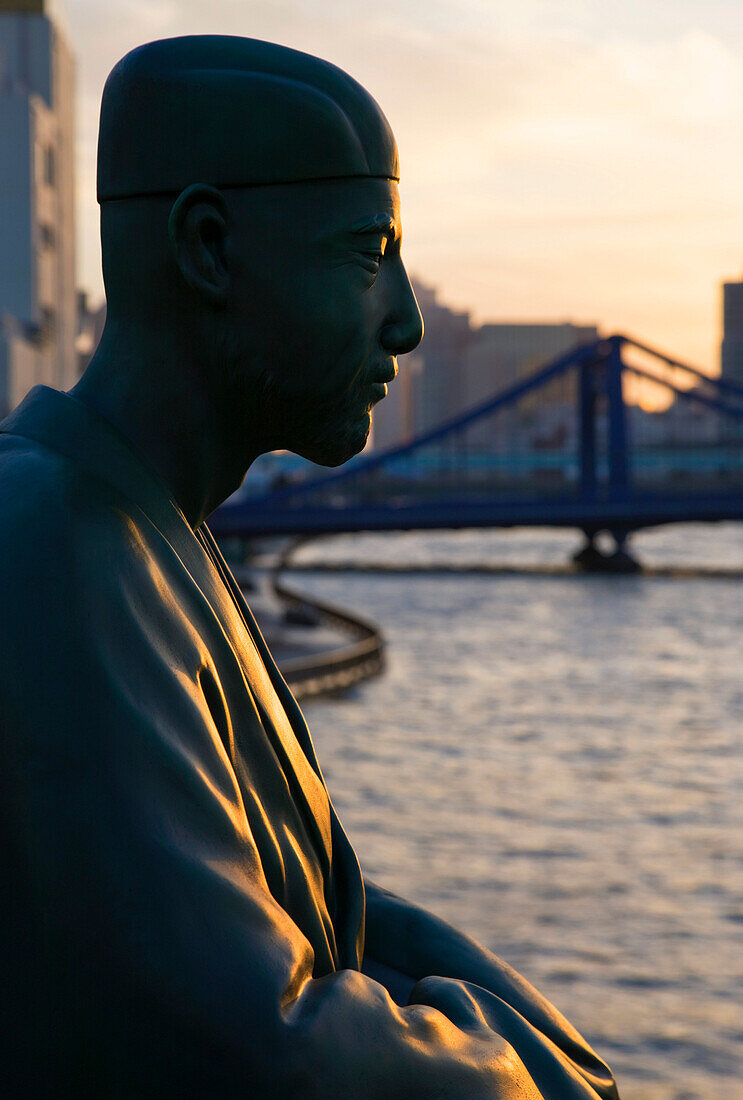 A statue of Matsuo Basho (Japan's most renowned haiku poet) overlooks the Sumida River and Kiyosubashi Bridge from the Basho-An Garden, located in the shitamachi downtown Koto-ku District of Tokyo, Japan.
