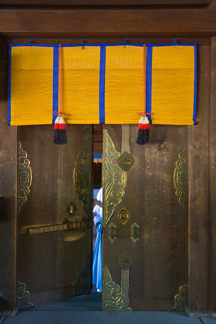 A detailed view reveals the fine craftsmanship in a wooden door with decorative metalwork and noren curtain inside the Outer Shrine of Meiji-Jingu Shrine, located in the Shibuya district of Tokyo, Japan.