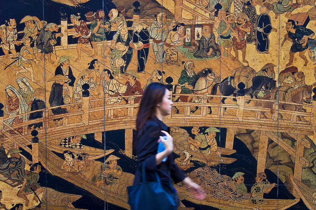 A young Japanese woman rushes by an old Edo-era woodblock print of the venerable Nihonbashi Bridge, which is being used as a mural for a construction site wall in the Nihonbashi district of central Tokyo, Japan.