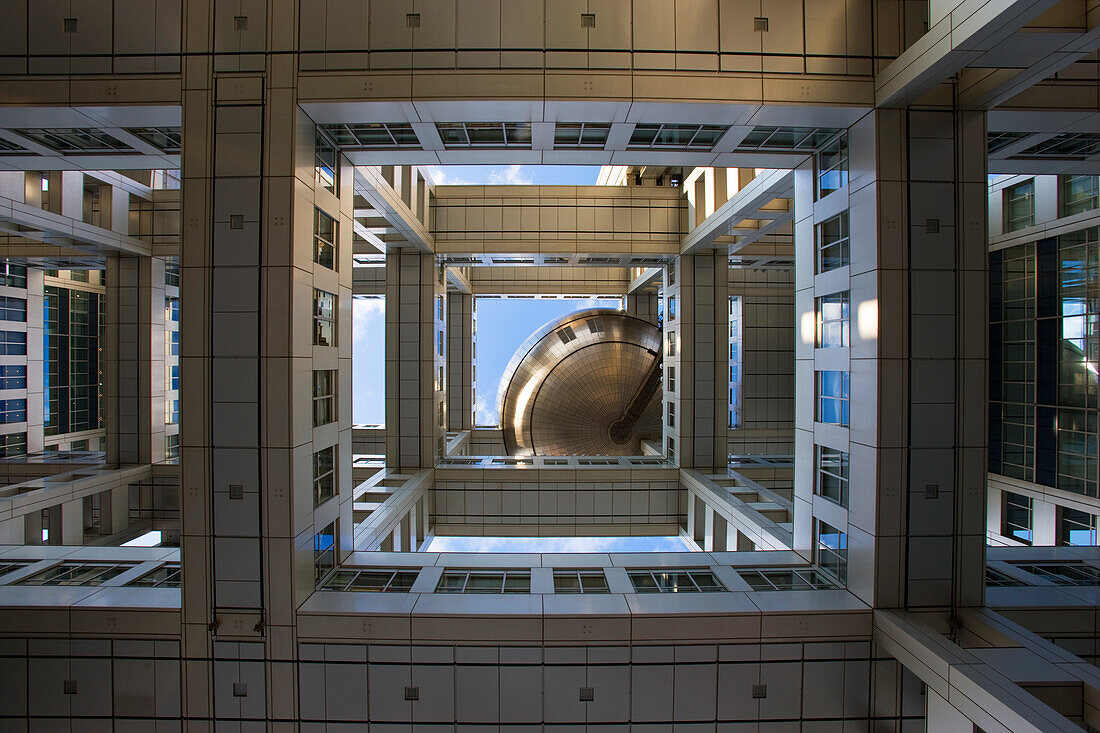 A low viewpoint looking skyward emphasizes the complex architectural structure leading up to the globe-shaped observatory of Fuji TV Headquarters in the Odaiba District of Tokyo, Japan.