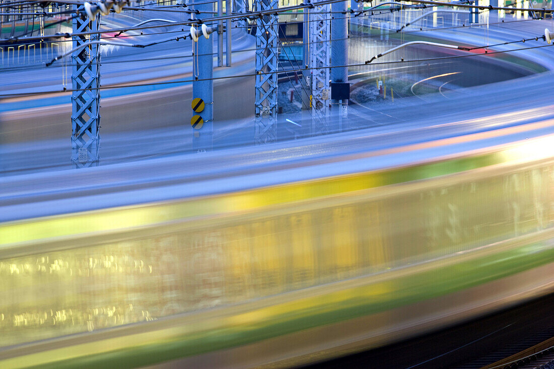 Commuter trains swing around the tracks curving into Ueno Station in Tokyo, Japan in this telephoto view using a slow shutter speed to capture the blurring motion of the passing trains.