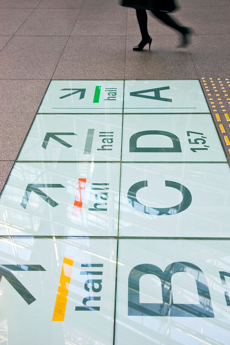 A detailed interior view reveals the laminated-glass and steel structure of the roof 60 meters above reflecting in directional signs imbedded in the floor of the Glass Building, the main entrance hall for the Tokyo International Forum (Japan's large [...]