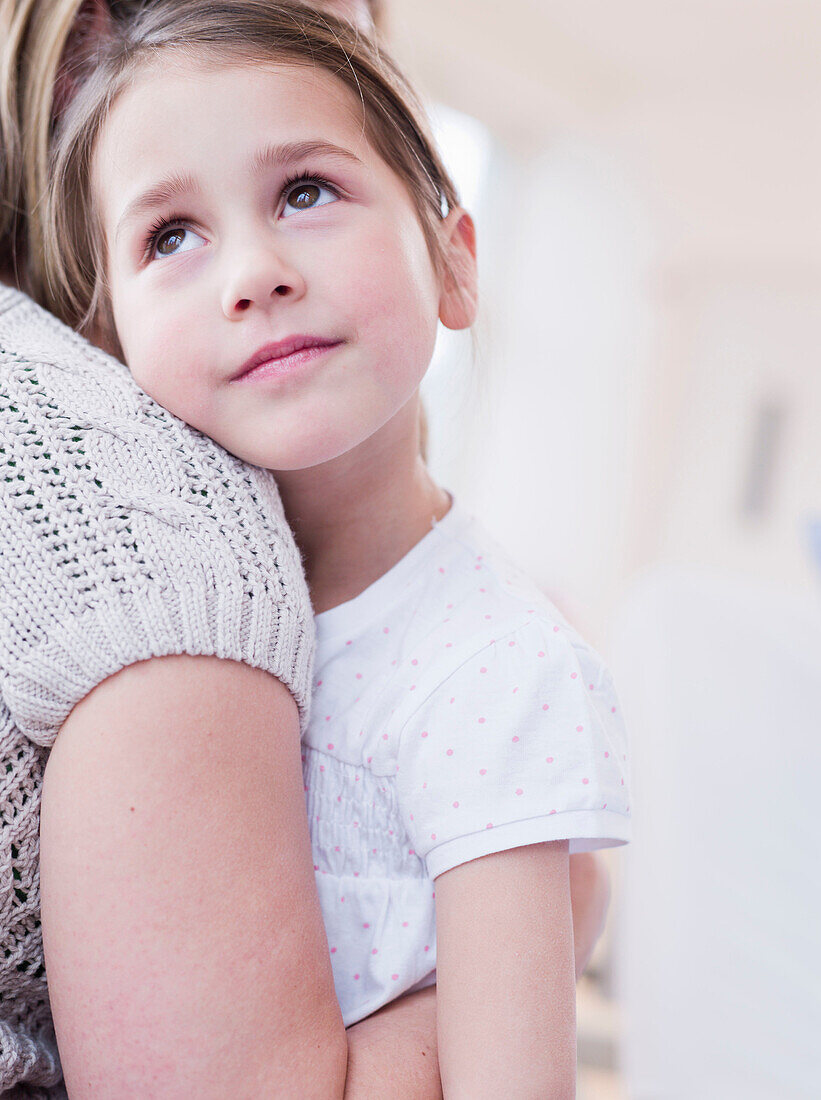 mother embracing her daughter. A mother in natural cotton shirt embracing her daughter, the girl with brown hair wearing a white shirt is looking upwards smiling