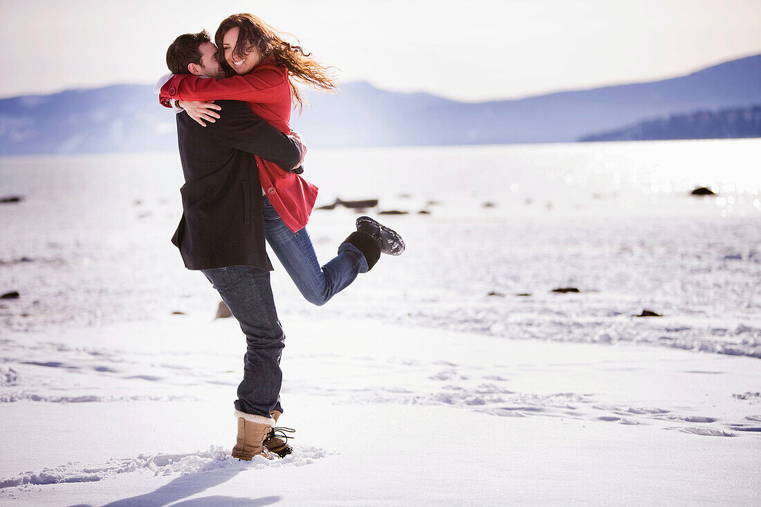 Man picking up woman on snowy beach