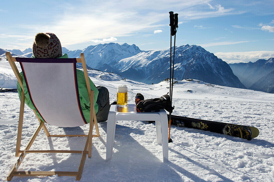 Skier relaxing with a beer. Skier relaxing with a beer on a deck chair on piste.