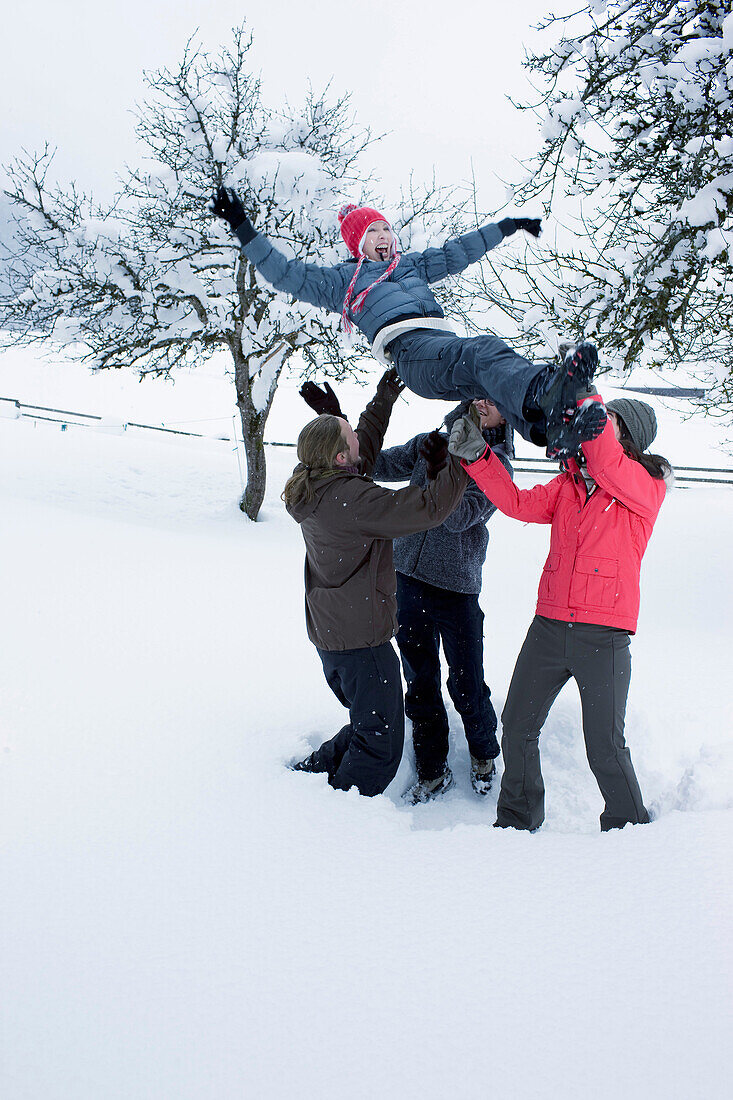 Young people having fun in the snow. Group of young people throwing a girl in the sky in snowy landscape smiling and laughing.