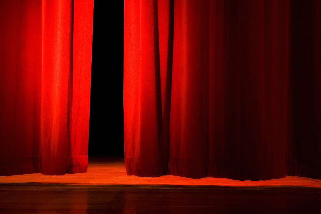 Lights on stage in theater. Red velvet curtains opening on lit stage in dark theater