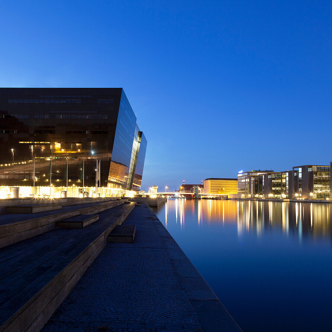 Lit buildings reflected in urban canal. Left: Royal Danish Library Det Kongelige Bibliotek, Black Diamond building, Copenhagen, Denmark