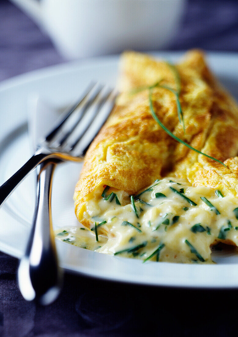 Close up of cheese omelette on plate. Chive and Cheese omelette withknife and fork on a white plate
