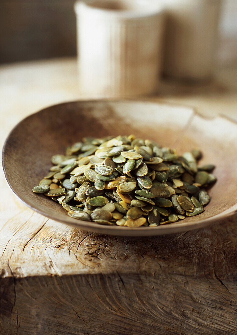 Wooden bowl of pumpkin seeds. Pumpkin Seeds in lightrustic wooden bowl on light rustic wooden surface