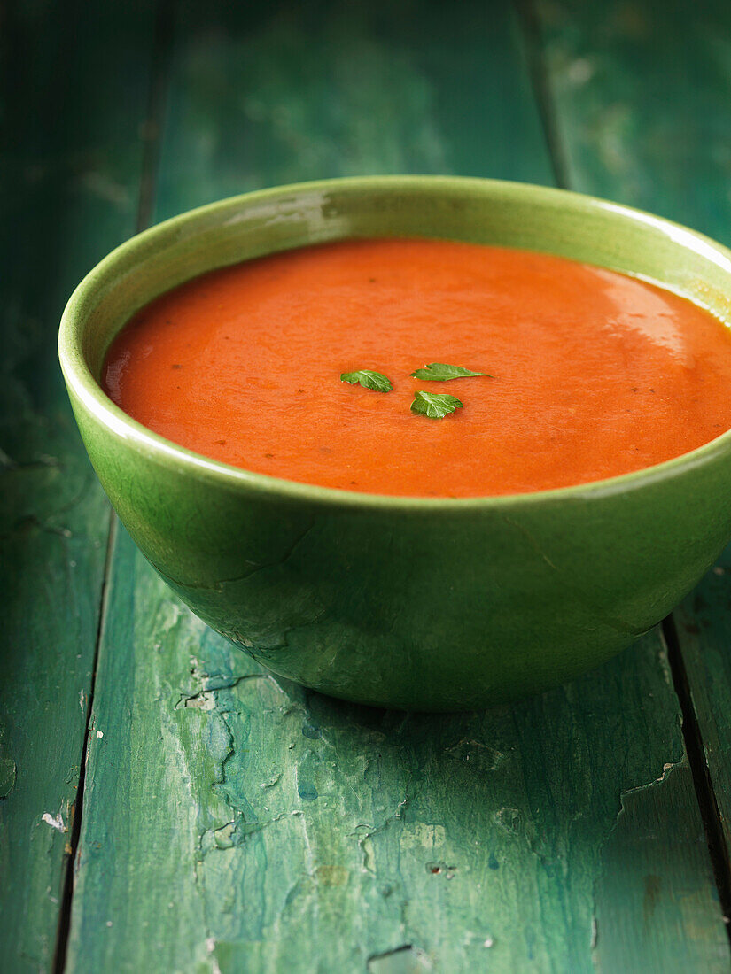 Close up of bowl of tomato soup. Tomato Soup in green bowl with a herb garnish