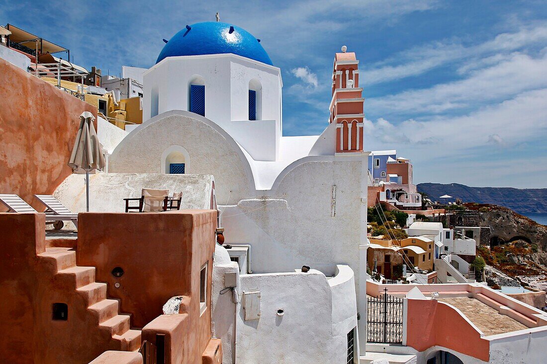 Blue domed church and salmon-colored deck overlooking ocean in the village of Oia in Santorini, Greece