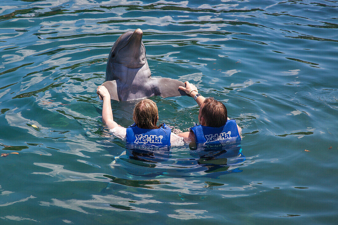 Zwei Besucher schwimmen mit einem Delfin im Delfinarium vom Xel-Ha Park, Tulum, Riviera Maya, Quintana Roo, Mexiko, Mittelamerika