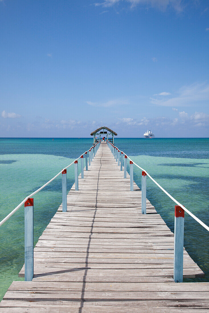 Ein Steg am Strand des Punta Frances Parque Nacional Nationalpark mit Kreuzfahrtschiff MS Deutschland (Reederei Peter Deilmann) auf Reede, Isla de la Juventud, Kuba, Karibik