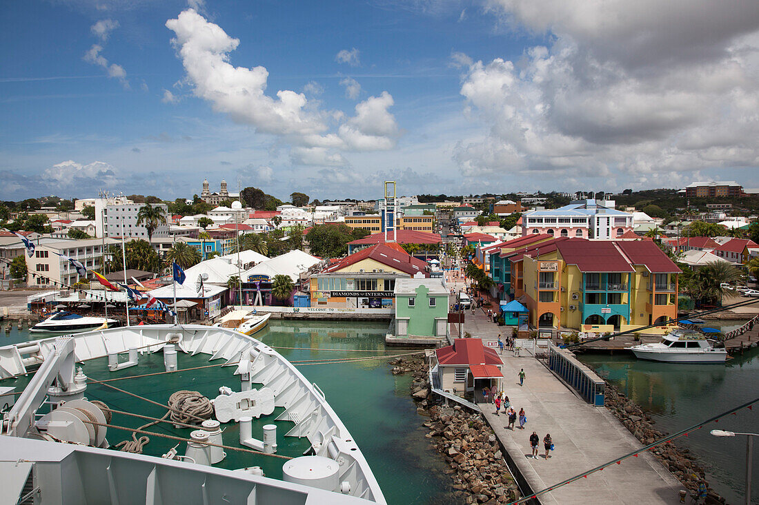 Bow of cruise ship MS Deutschland (Reederei Peter Deilmann) at a pier with colorful houses and shops near the port, St. John's, St. John, Antigua, Antigua and Barbuda, Caribbean