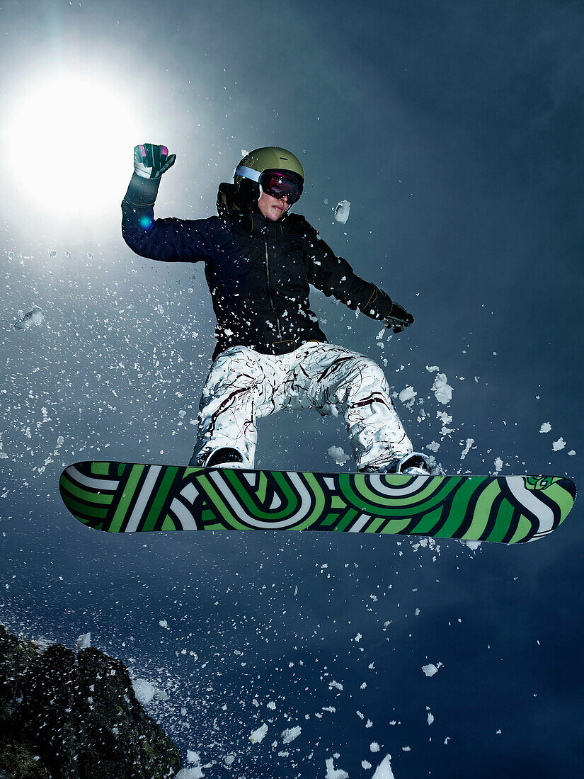 Female snowboarder jumping over rock