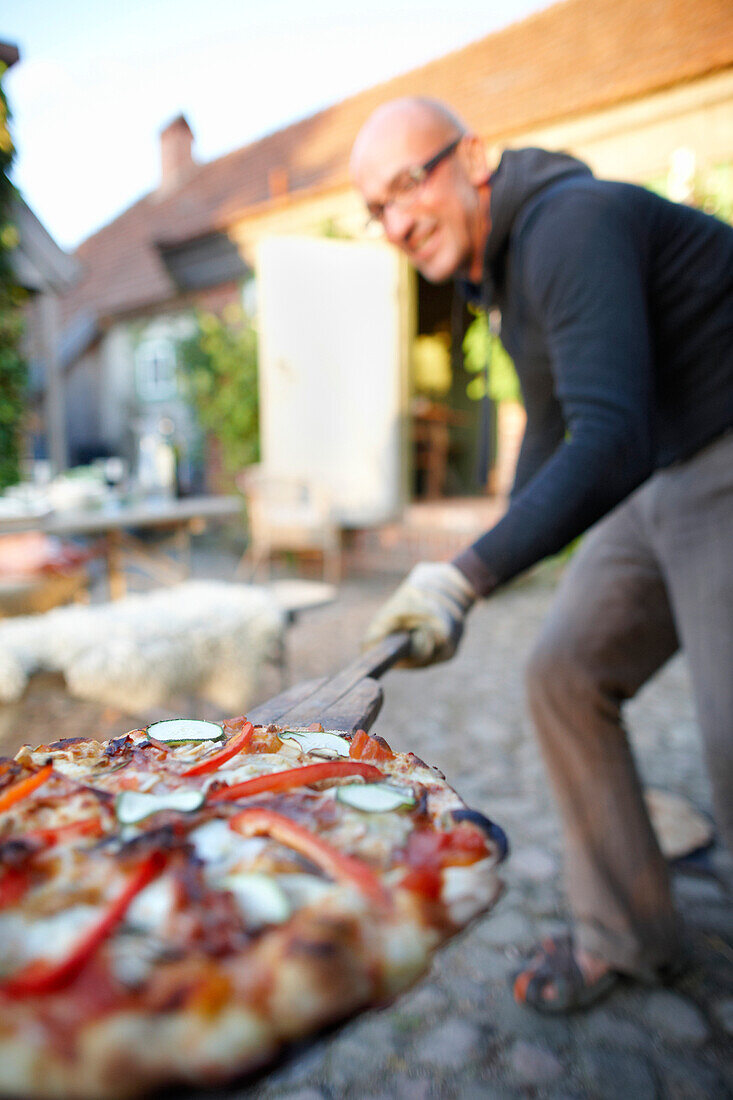 Mann trägt Pizza auf einer Brotschaufel, Haus Strauss, Bauernkate in Klein Thurow, Roggendorf, Mecklenburg-Vorpommern, Deutschland