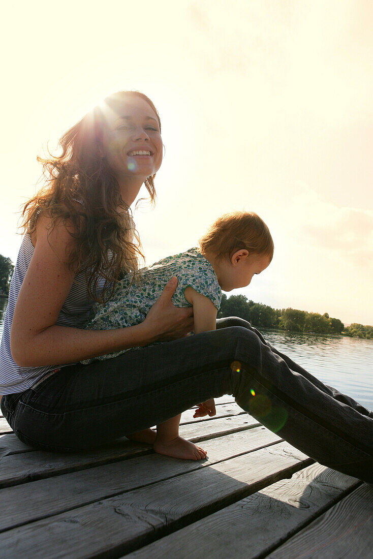 Woman with small child, sitting on wooden pier, old danube, Vienna, Austria