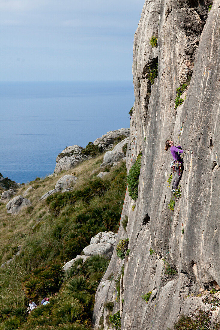 Junge Frau klettert in steiler Wand, Wandern und Klettern auf Mallorca, Klettergebiet am Cap de Formentor, Blick auf das Mittelmeer, La Creveta, Cap de Formentor, Serra de Tramuntana, Unesco World Cultural Heritage, Mallorca, Spanien