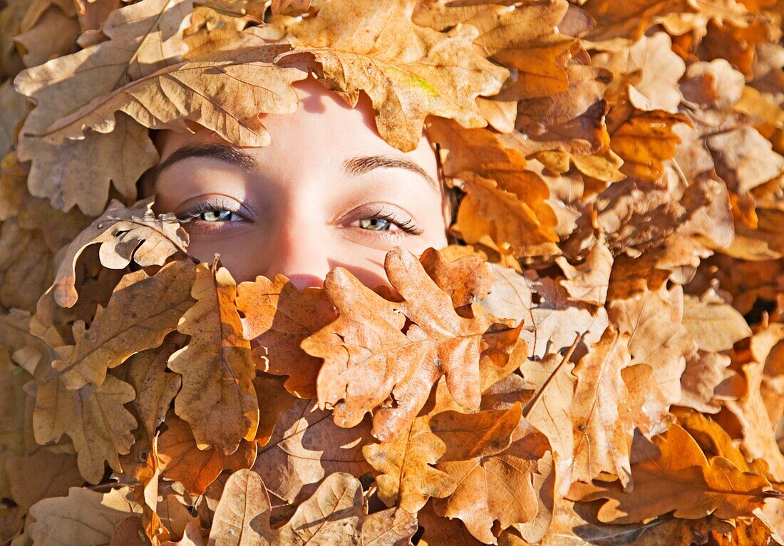 Portrait of a woman covered form leafes in Park in Autumn