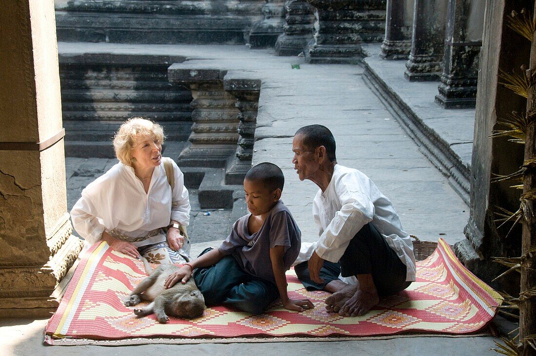 Asia, Cambodia,  Siem Reap , Angkor Wat, woman tourist with father his son and monkey seated on a carpet in courtyard of temple.