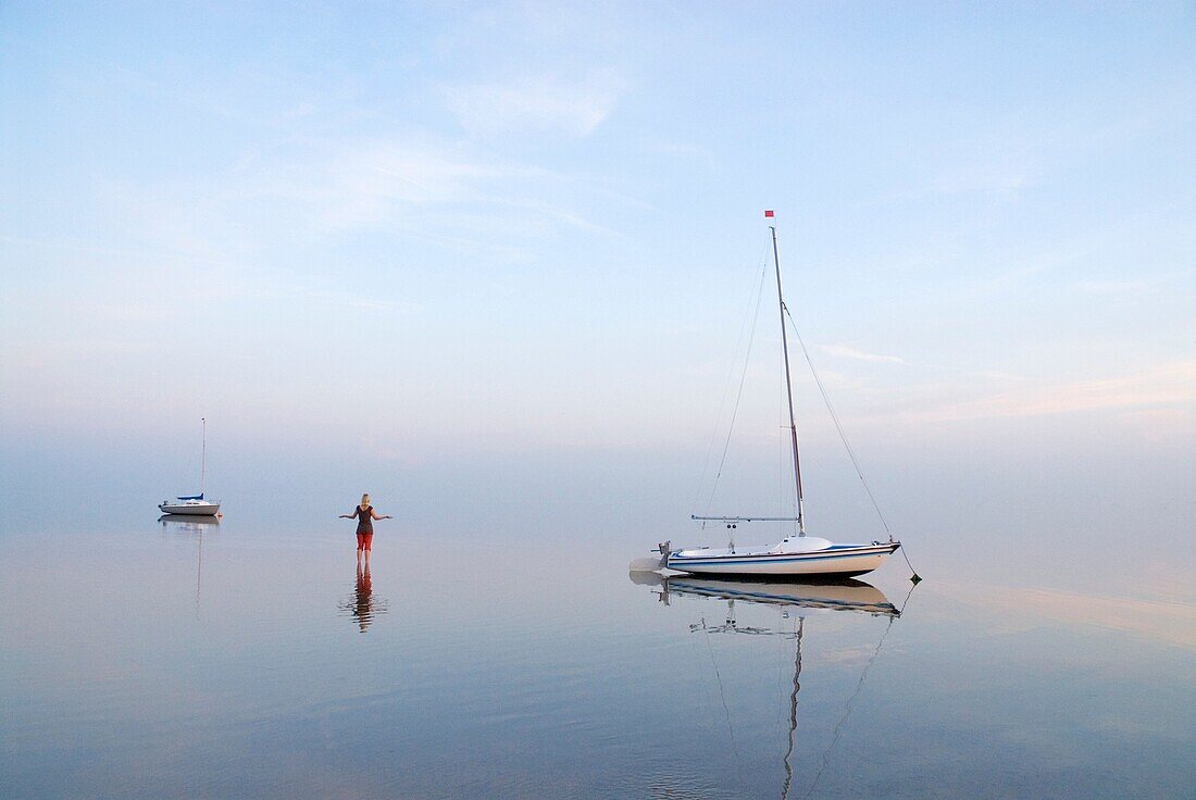 Woman standing among sailboats in Wadden Sea at sunset, Juist, Germany