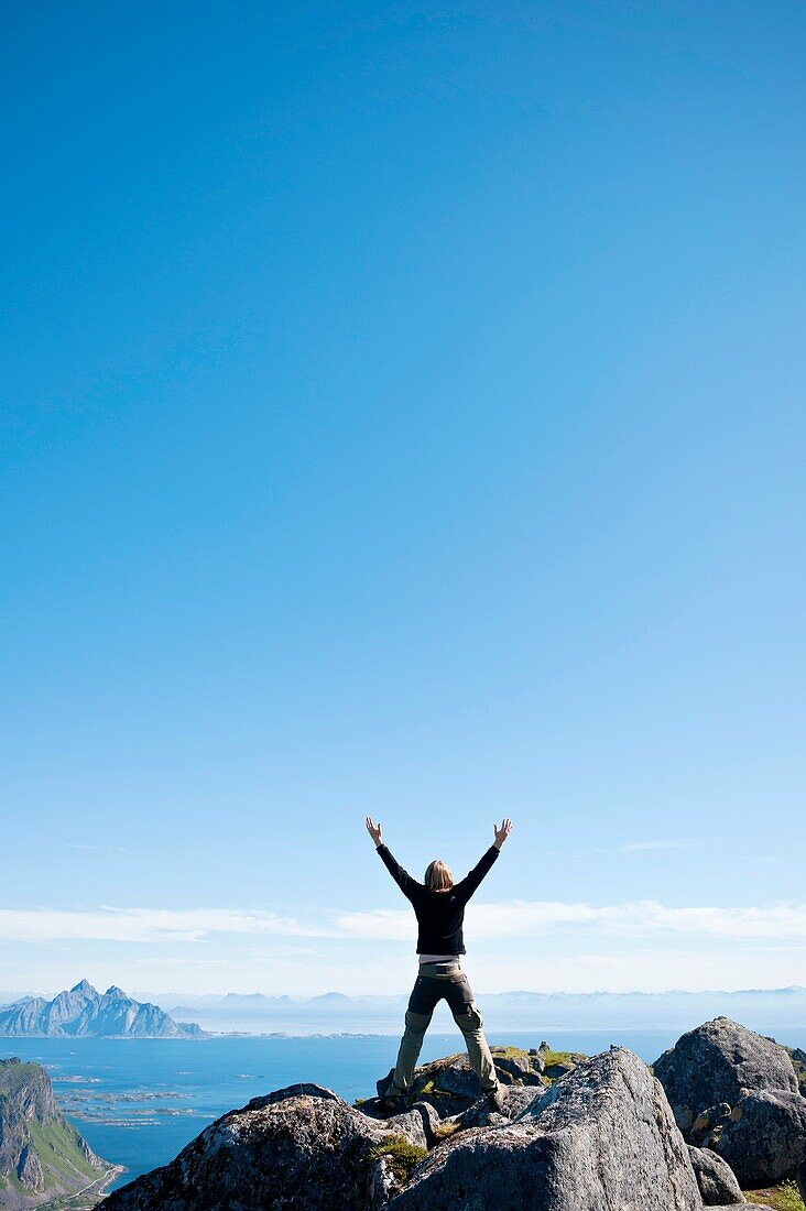 Hiker stands in celebration on summit of Justadtind, Lofoten islands, Norway