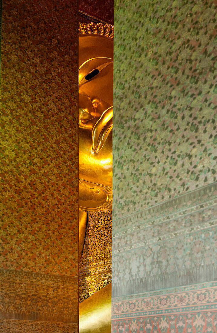Glimpse of the reclining Buddha at Wat Pho temple. Head and arm. Seen through a gap in the mosaic covered pillars. Gilded statue., Bangkok, Thailand. Statue of a reclining Golden Buddha