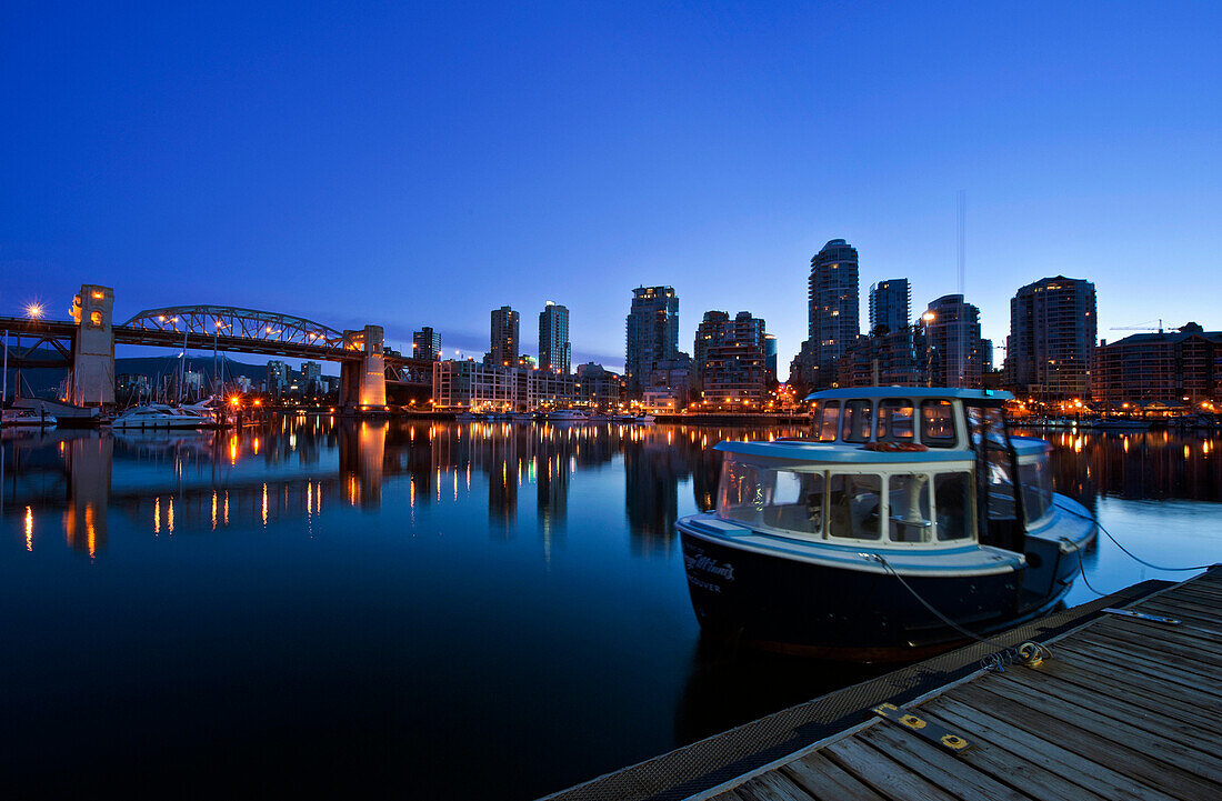 False Creek Ferry at Dawn. The Vancouver skyline at twilight or dawn, with low light and blue sky, and flat calm water. Lit up skyline and tall buildings. British Columbia, Canada., False Creek Ferry at Dawn