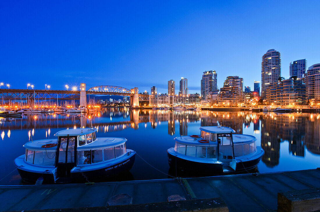 Granville Island at Dawn. The Vancouver skyline at twilight or dawn, with low light and blue sky, and flat calm water. Lit up skyline and tall buildings. British Columbia, Canada., Granville Island at Dawn