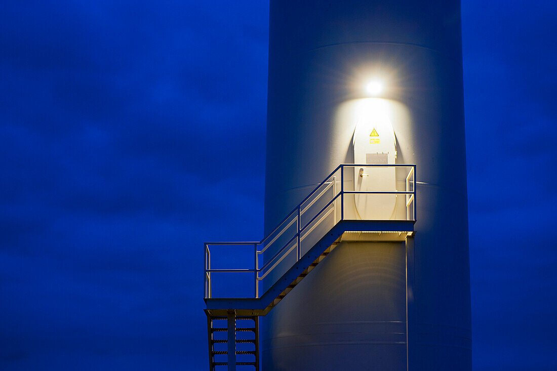 The light above the maintenance door illuminating the staircase on the side of the central mast of a wind turbine. Night. Wind power generation., Wind Turbine Maintenance entrance