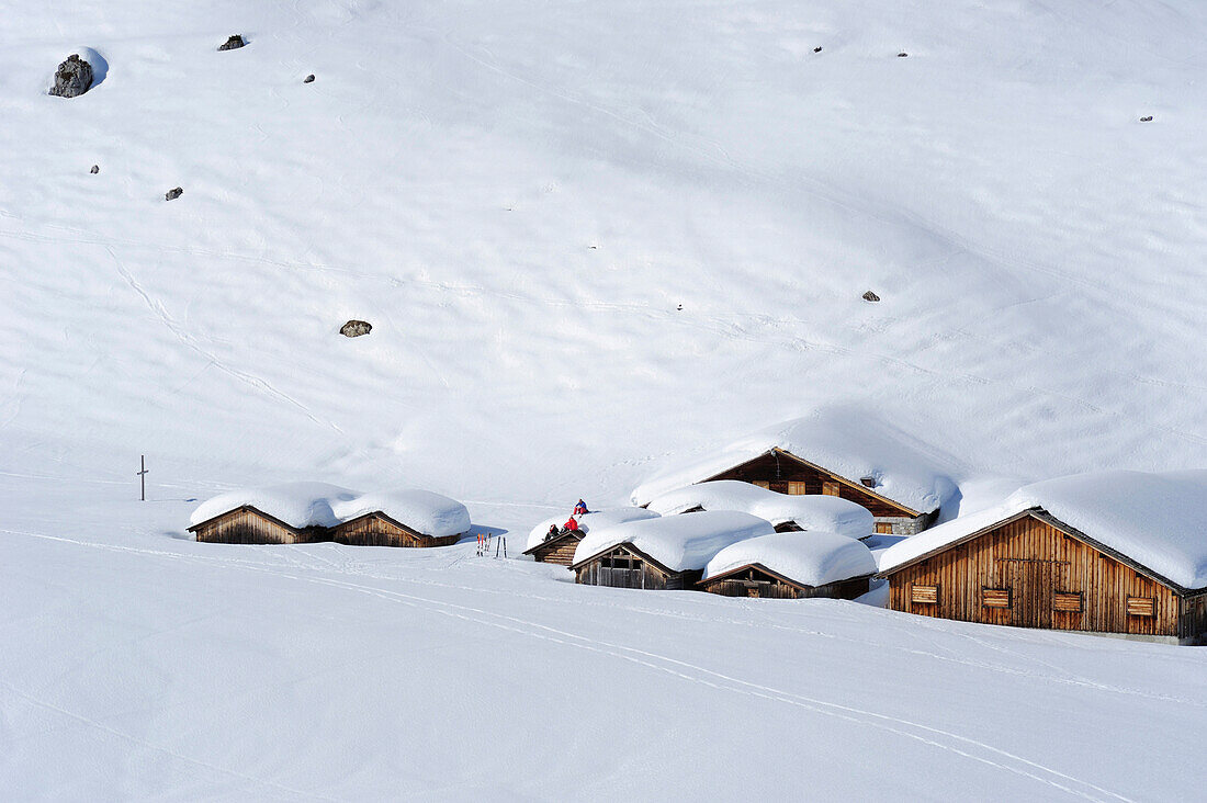 Drei Skitourengeher sitzen auf Dächern von verschneiten Almhütten, Rätikon, Montafon, Vorarlberg, Österreich