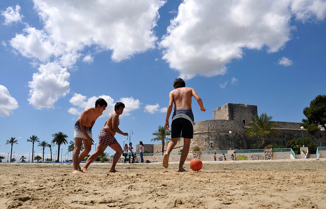Drei Teenager beim Fußballspielen am Strand, Castello in Manfredonia am Gargano, Apulien, Italien