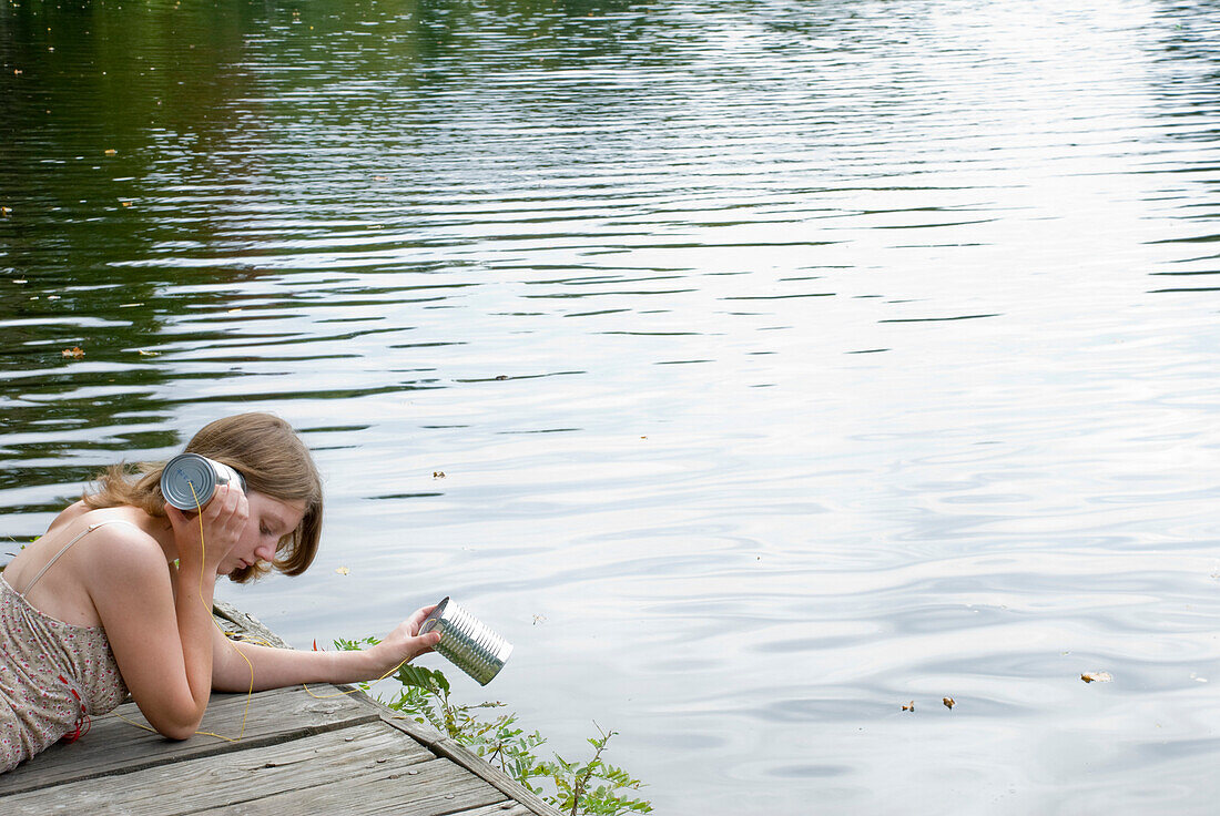 Young Woman Listening to Tin Can at Water's Edge