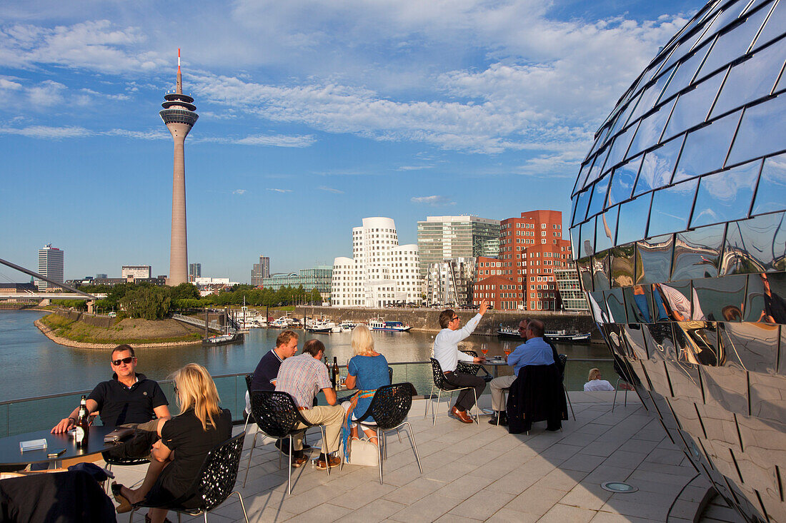 People at the terrace of a restaurant at media harbour, view to Rhine tower and Neuer Zollhof, Duesseldorf, North Rhine-Westphalia, Germany, Europe