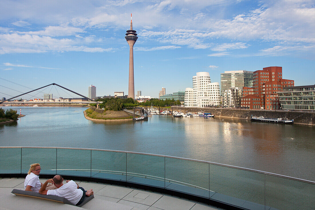 Couple sitting on a terrace at media harbour, view o Rhine tower and Neuer Zollhof with Gehry buildings, Duesseldorf, North Rhine-Westphalia, Germany, Europe
